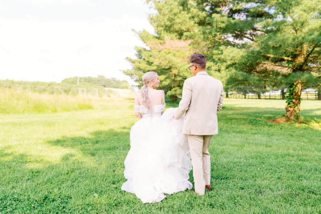 candid photo of the bride and groom walking at a lake around farm grounds 