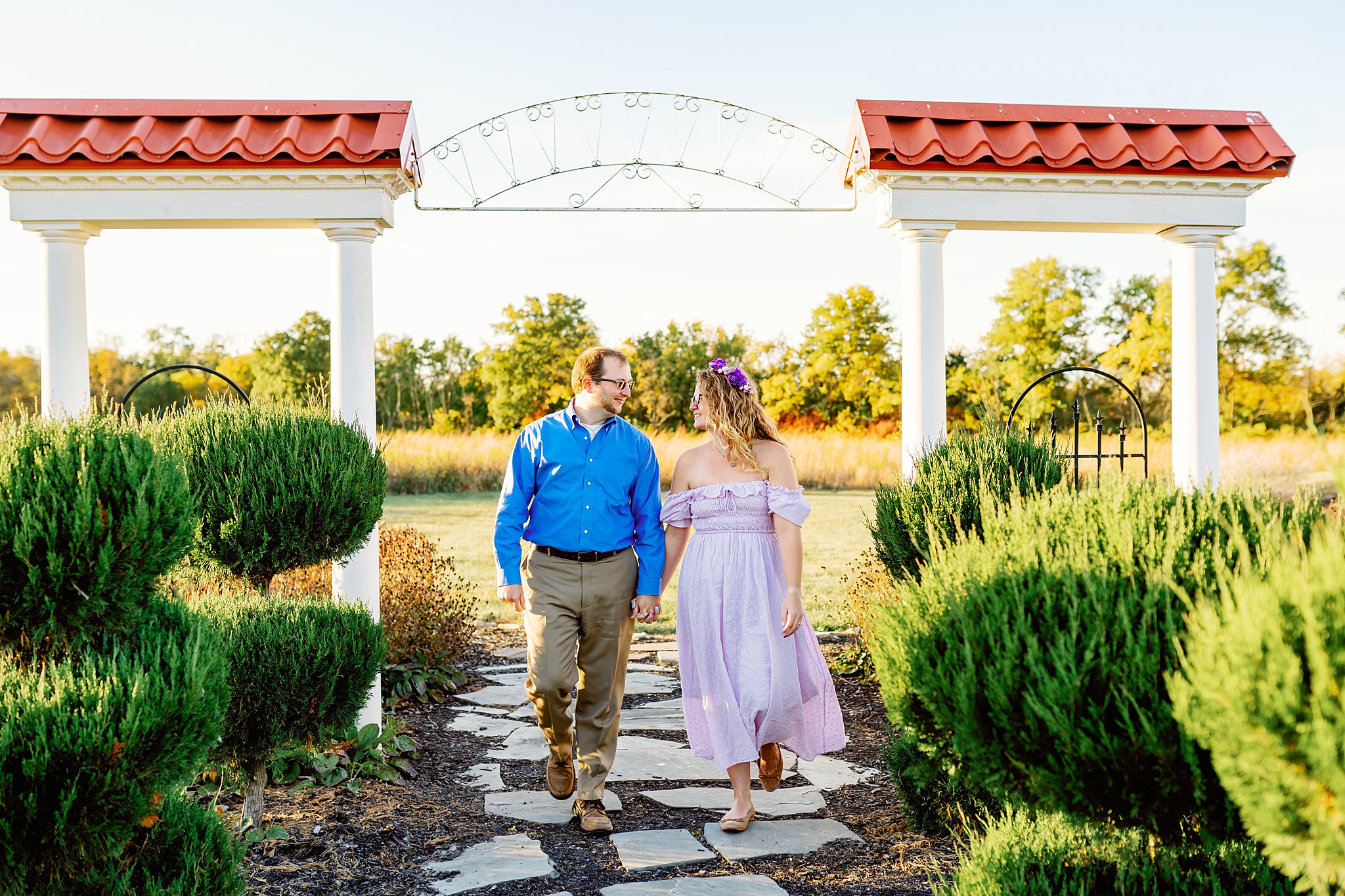 A young couple walks along a stone path under columns archway in a garden places to take pictures in dayton ohio