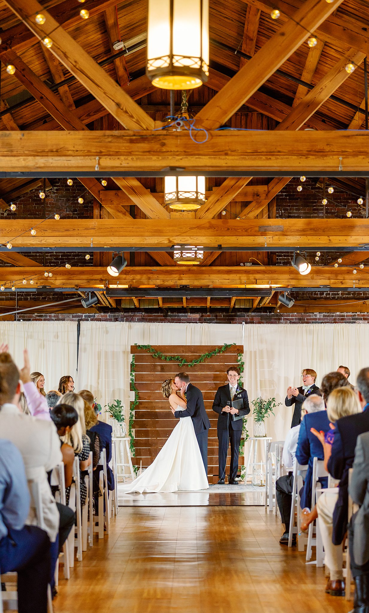 Newlyweds kiss for the first time in a cerermony taking place in a large wooden barn