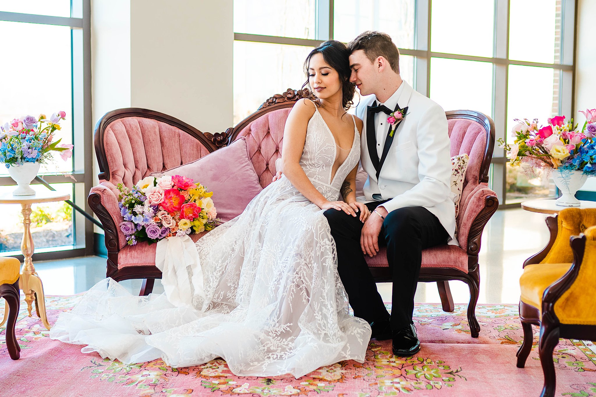 Newlyweds sit on a pink antique couch in a room with large windows and colorful flowers unique wedding venues dayton ohio
