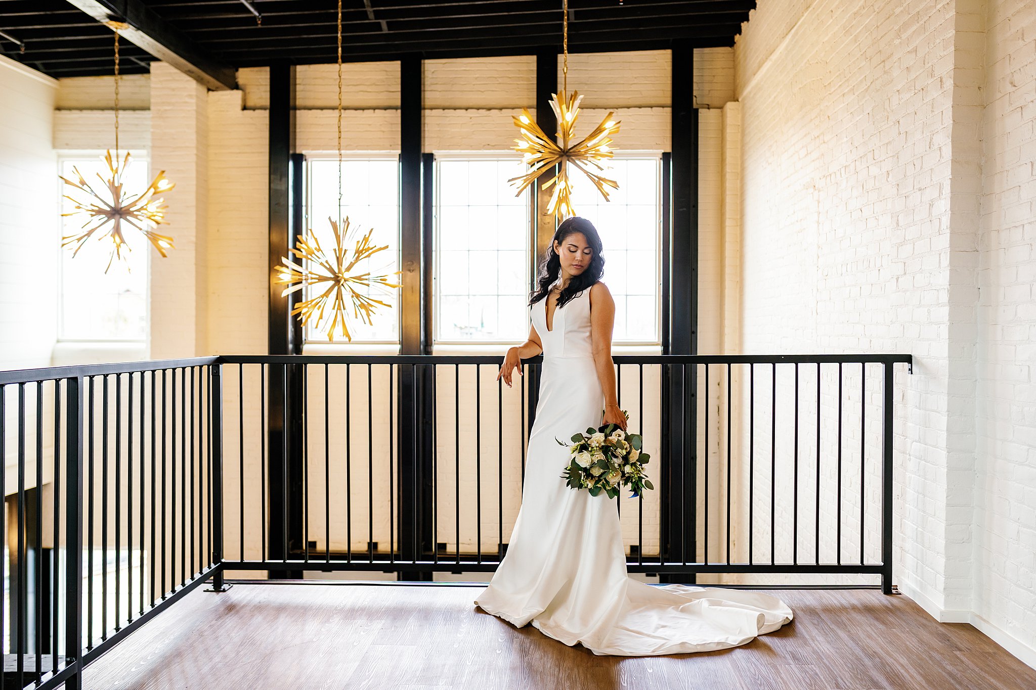Bride stands in her dress on an indoor balcony in front of large windows and modern chandeliers unique wedding venues dayton ohio